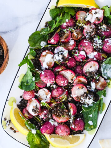 roasted radish salad with black lentils, dressing on white marble.