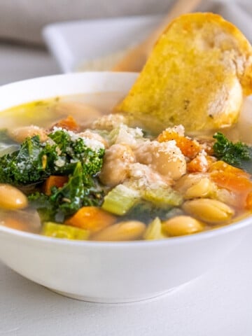 tuscan white bean soup with kale in white bowl and bread